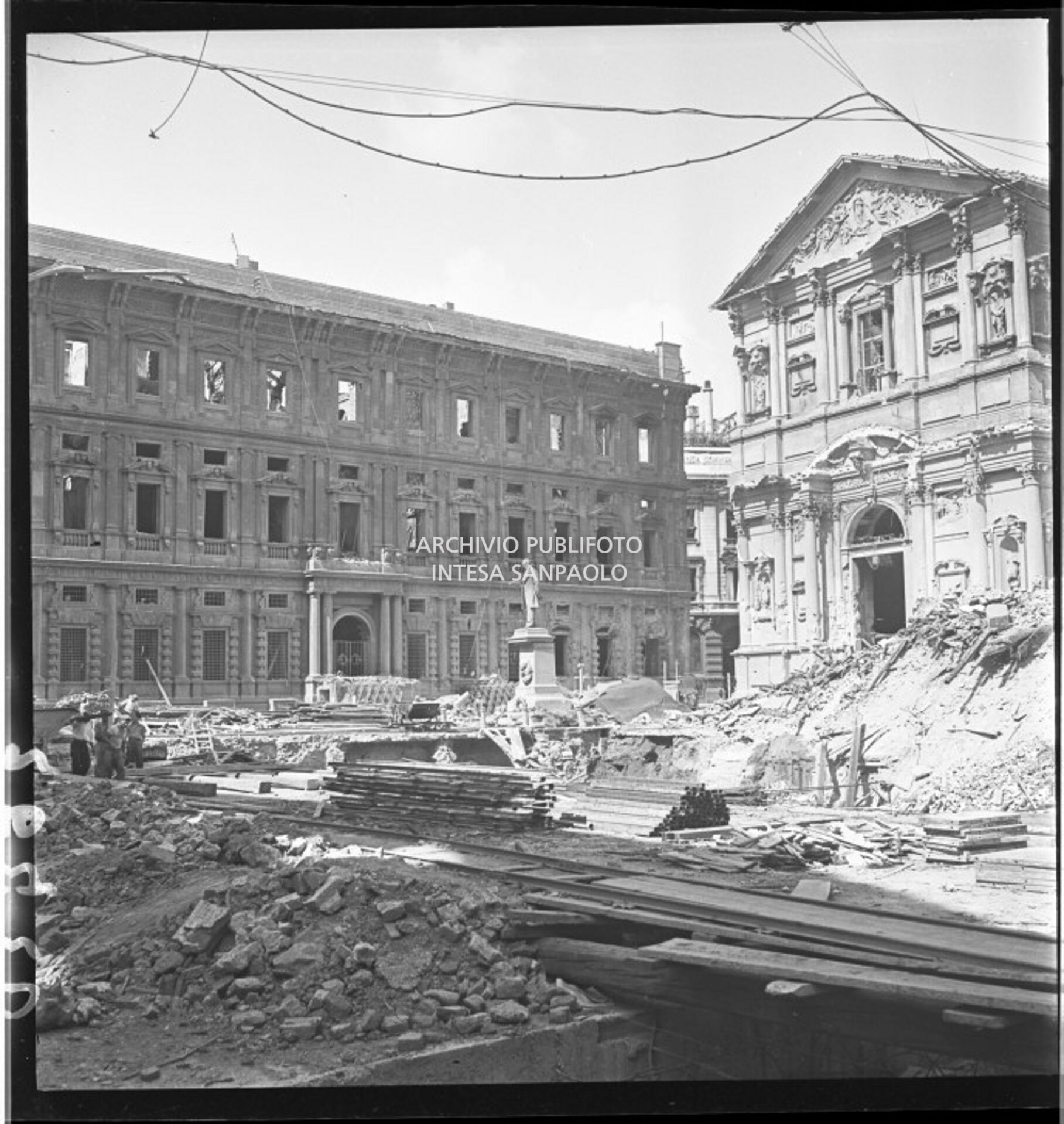 Piazza San Fedele a Milano ingombra delle macerie dei bombardamenti: sullo sfondo la facciata posteriore di Palazzo Marino, a destra la chiesa di San Fedele entrambi gravemente danneggiati dagli attacchi aerei. In mezzo alla piazza il monumento ad Alessandro Manzoni intatto
